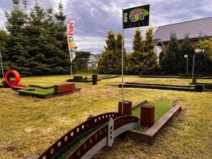 Un parcours de minigolf avec un obstacle circulaire rouge, un pont et des drapeaux.