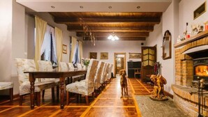 A dining area with a long wooden table and chairs, a fireplace, and a dog standing in the center. - Large Holiday Villa With Garden, 6 Bedrooms (Łobez)