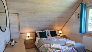 A cozy bedroom with a sloped ceiling, a bed with floral bedding, two bedside lamps, a small table, and a window with curtains. - Cottage in a Quiet Location, Slajszewo (Choczewo)