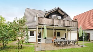 Uma casa de dois andares com um deck de madeira, varanda e área de jantar com mobiliário para exterior.