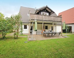 A two-story house with a wooden deck, a balcony, and a dining area with outdoor furniture.