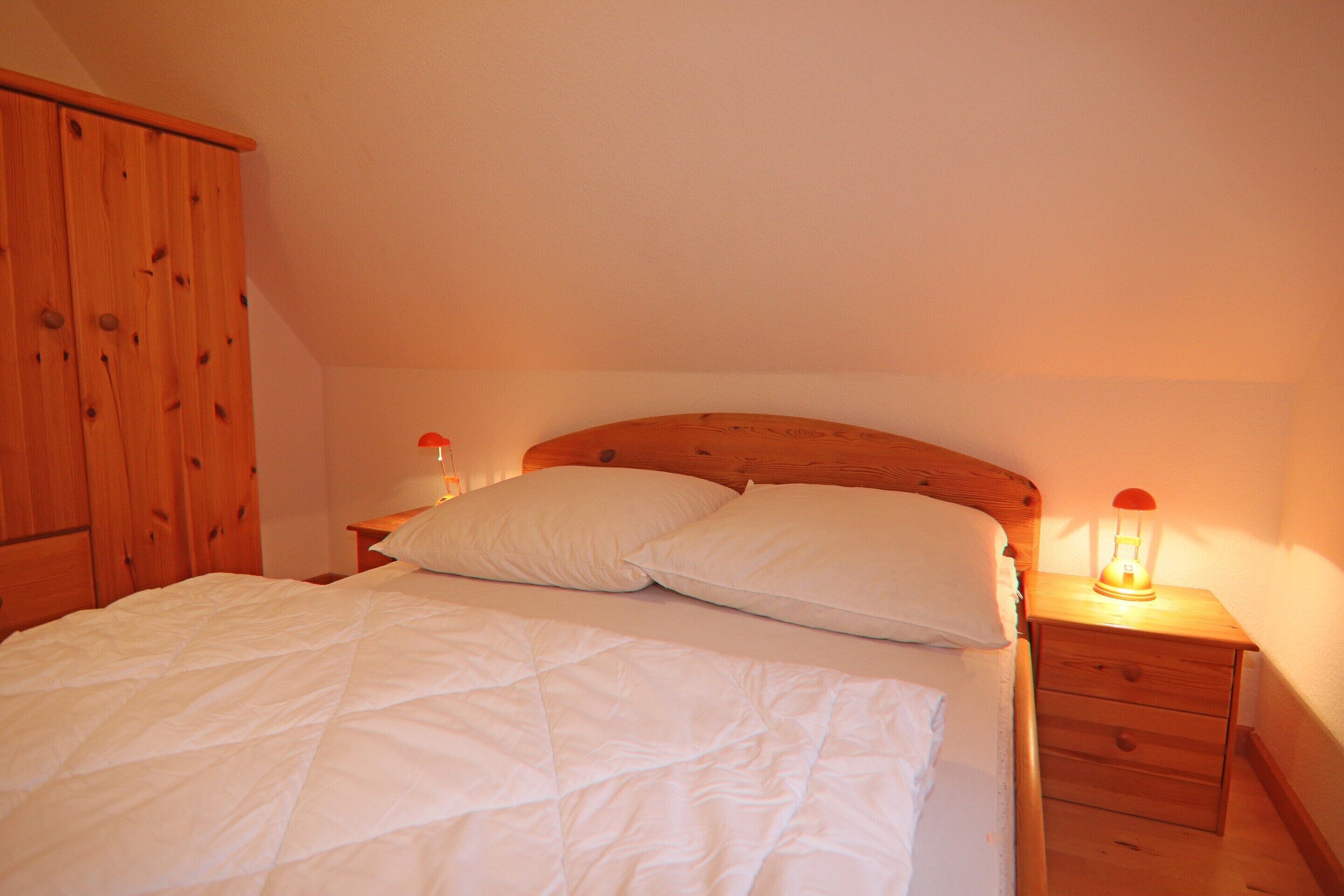 Une chambre à coucher avec une tête de lit en bois, un lit avec une literie blanche, deux tables de chevet avec des lampes et une armoire en bois.