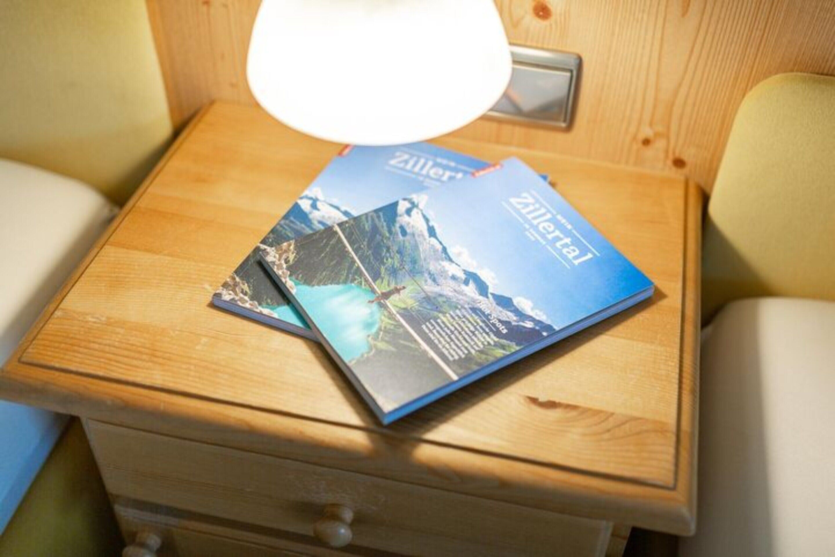 A wooden bedside table with a lamp and two Zillertal brochures.