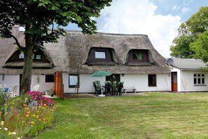 A thatched-roof cottage with a garden, outdoor seating, and a white exterior wall. - Holiday Home on the Dike, Busum (Westerdeichstrich)