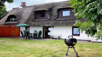 A house with a thatched roof, a patio with chairs and a table, and a barbecue grill in the yard.