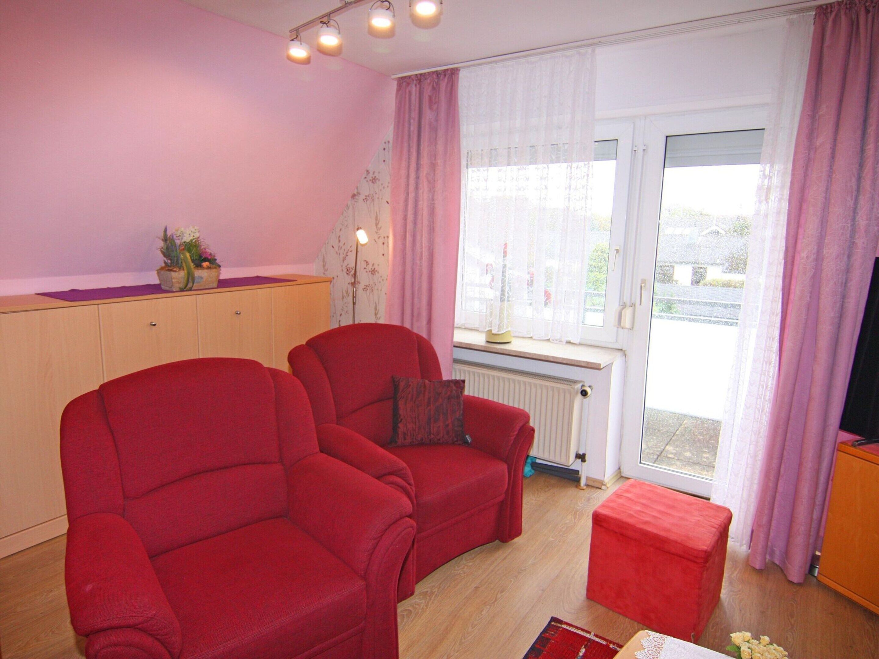 Un salon avec deux fauteuils rouges, un petit pouf, un meuble en bois et un radiateur.