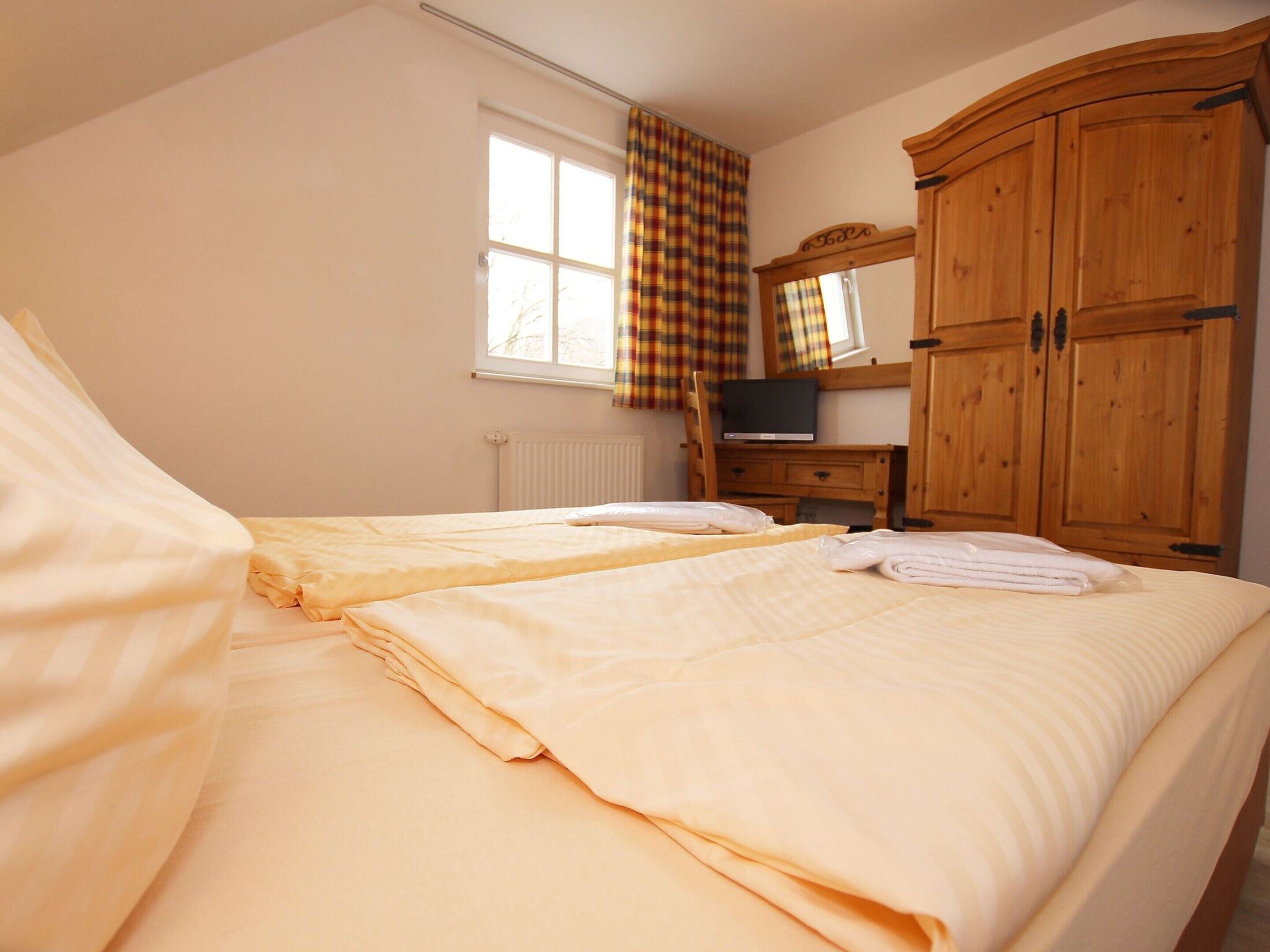 A bedroom with two beds, a wooden wardrobe, a radiator, and a window with curtains.