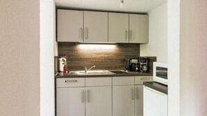 Eine kompakte Küche mit modernem Design, ausgestattet mit einer eingebauten Mikrowelle, einer Kaffeemaschine und einem Spülbecken mit Armatur.