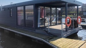 A modern floating structure with large windows, a covered deck, and lifebuoys. - Houseboat in Kamien Pomorski (Kamien Pomorski)