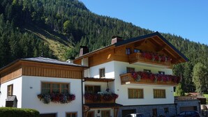 A two-story building with wooden balconies and flower boxes, surrounded by a mountainous landscape. - Apartment in Flachau Near Ski Slopes (Flachau)