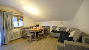 A cozy living room with a wooden dining table, two chairs, a grey sofa, and a black throw blanket. - Apartment in Flachau Near Ski Slopes (Flachau)