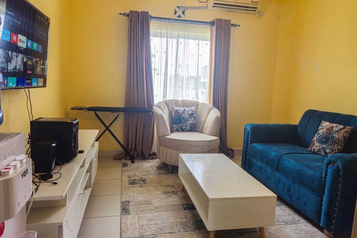 A living room with a sofa, armchair, and a TV mounted on the wall.