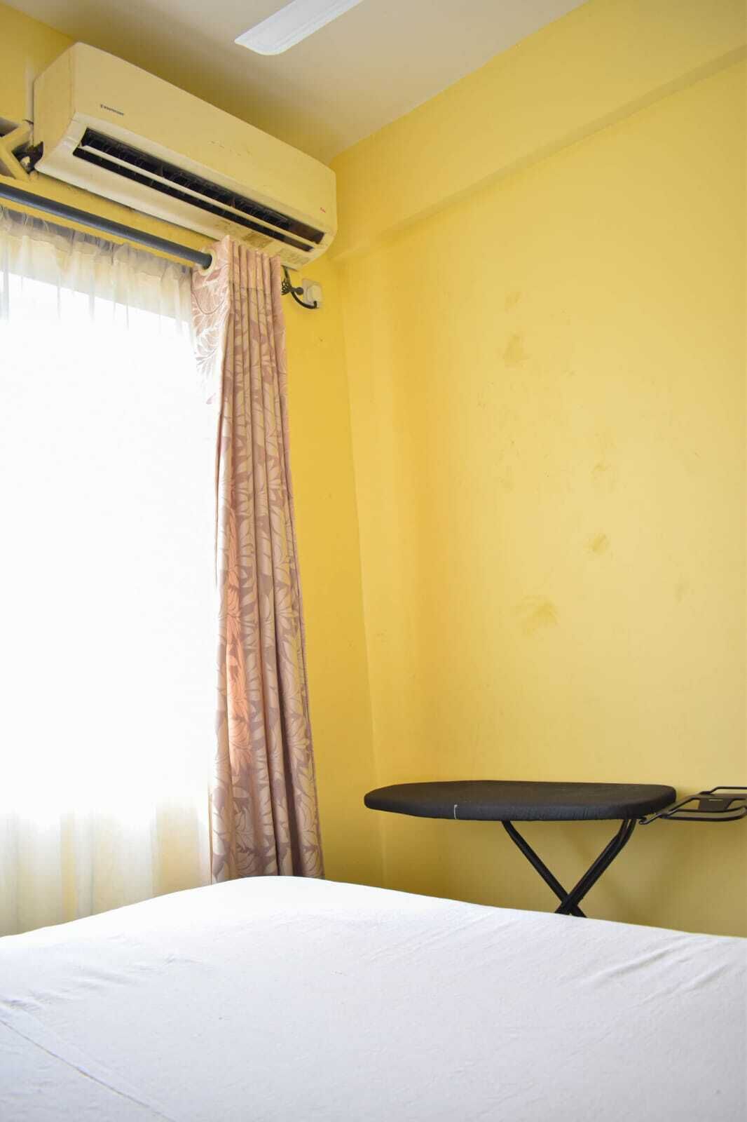 Una habitación con cama, aire acondicionado, una mesita y una cortina.