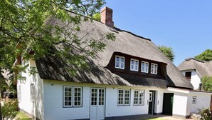 Une petite maison blanche au toit de chaume, avec un petit porche et une porte.