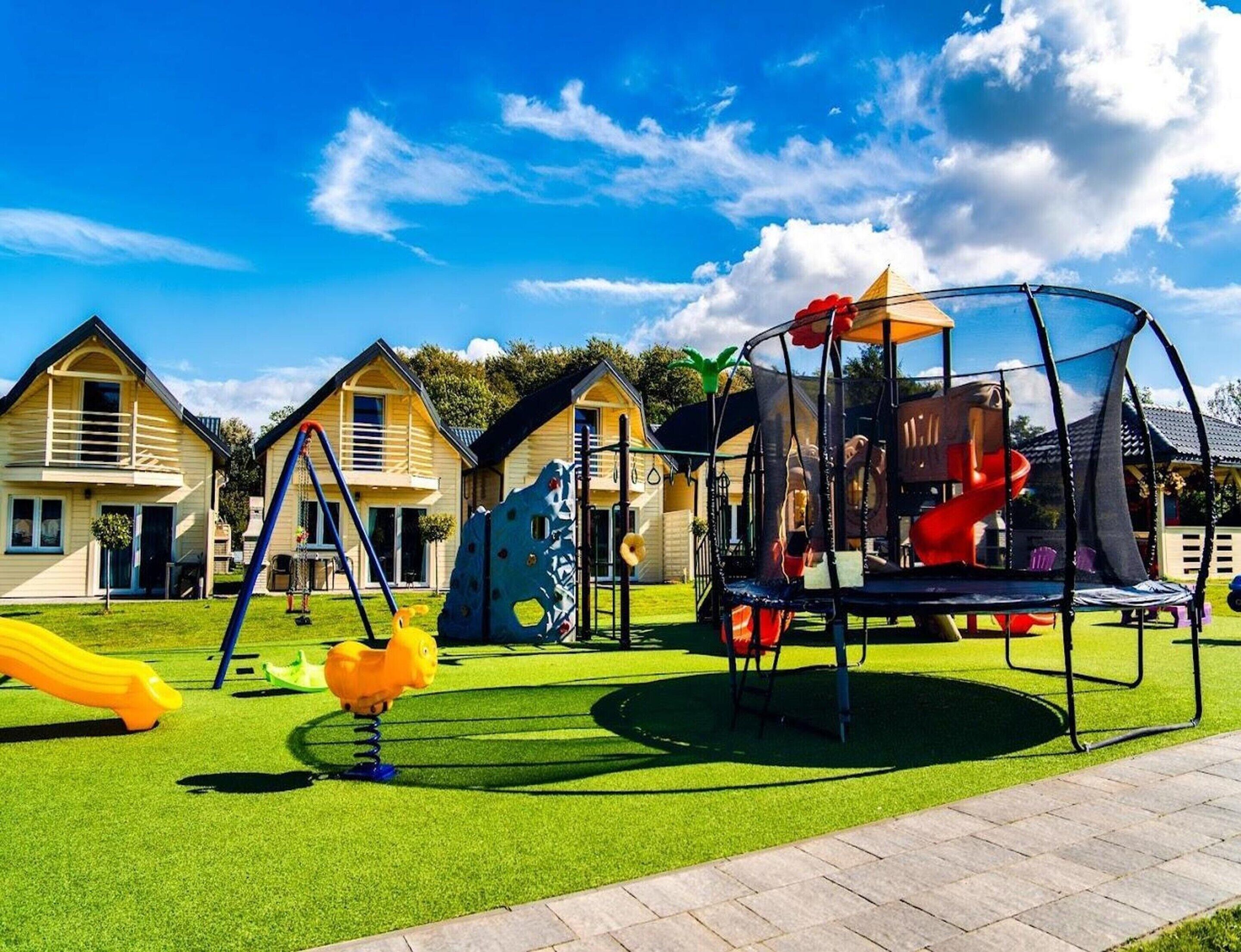 A playground with a trampoline, slides, and climbing structures, surrounded by houses.
