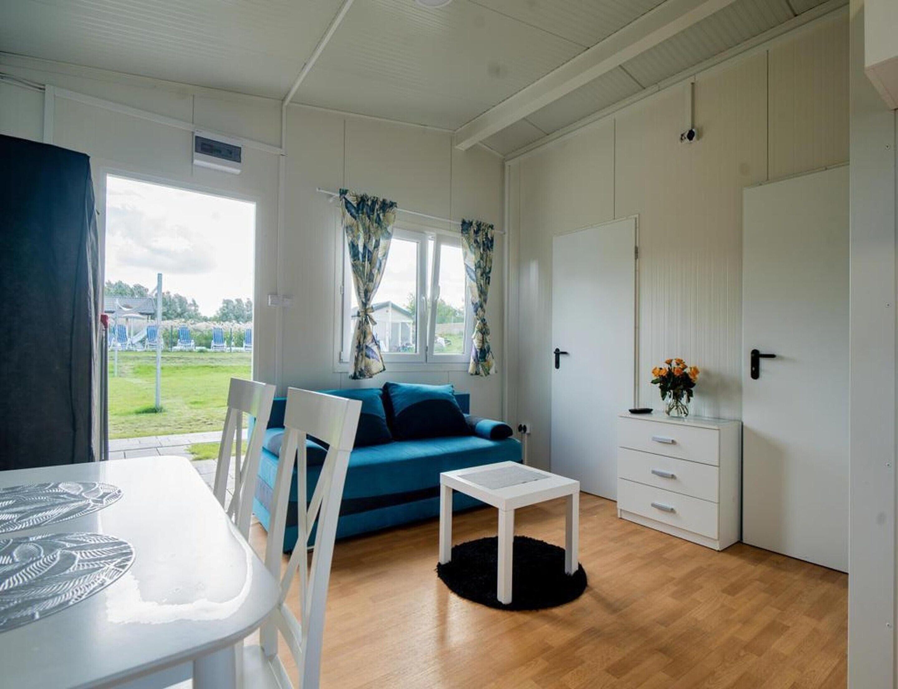 A room with a blue sofa, white furniture, a small table, and a view of a grassy area outside.