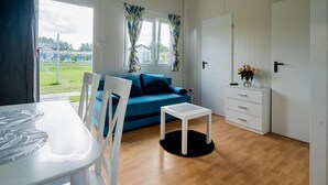 A room with a blue sofa, white furniture, a small table, and a view of a grassy area outside. - Single-story Holiday Home, Pool, Jacuzzi (Ustronie Morskie)