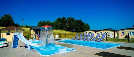 A swimming pool with a water slide and lounge chairs.