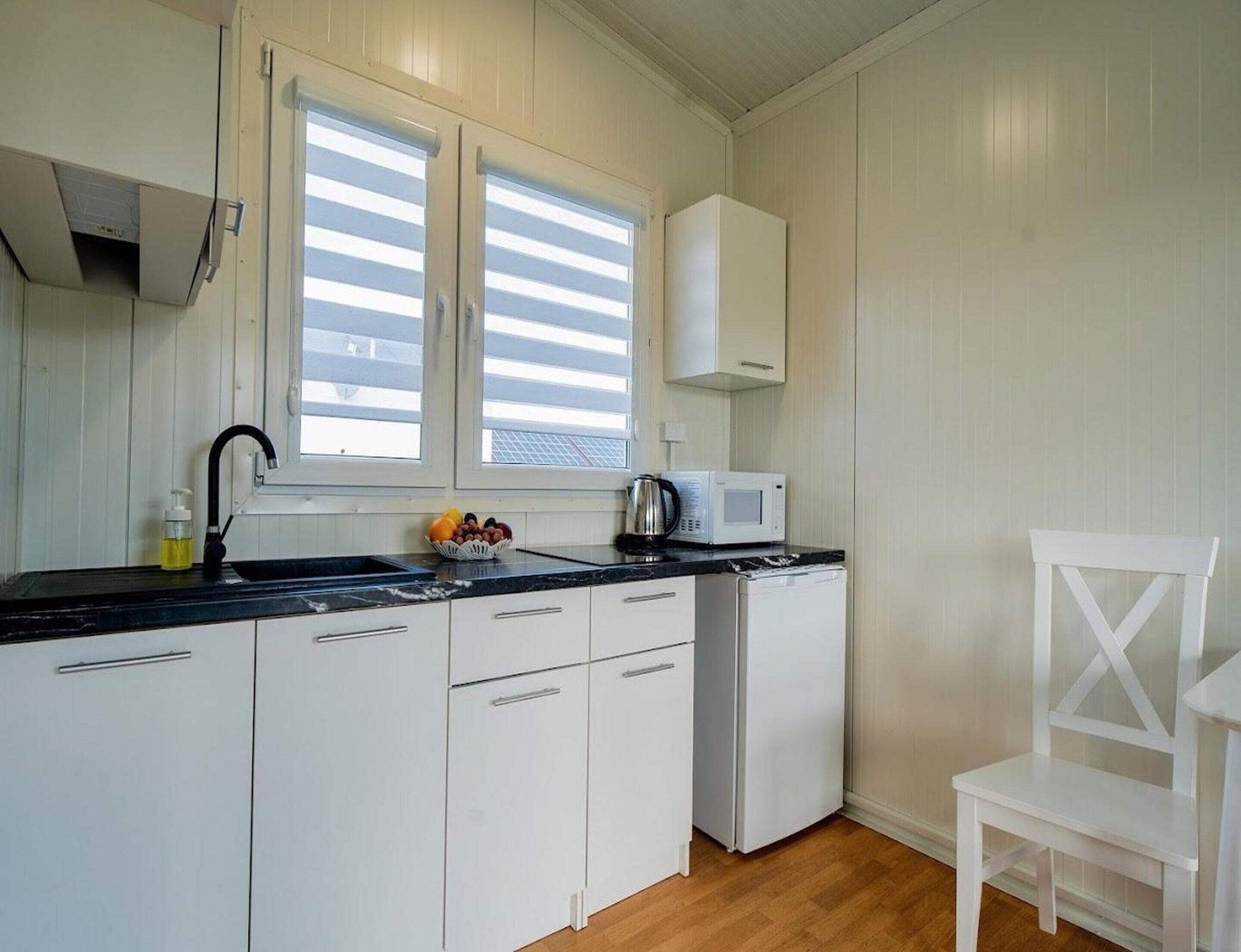 A kitchen with white cabinets, a black countertop, a microwave, and a white chair.
