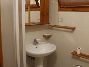 Ein Badezimmer mit einem weißen Waschbecken, einem Spiegel darüber und Holzregalen.