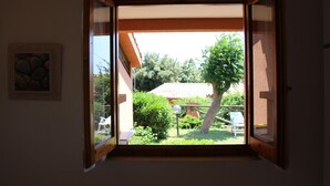 Ein Zimmer mit offenem Fenster und Blick auf einen Garten, einem gerahmten Bild an der Wand und einer Decke mit einem gemusterten Design.