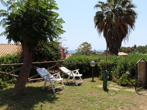 Ein Garten mit zwei weißen Liegestühlen, einer Palme und Blick aufs Meer.