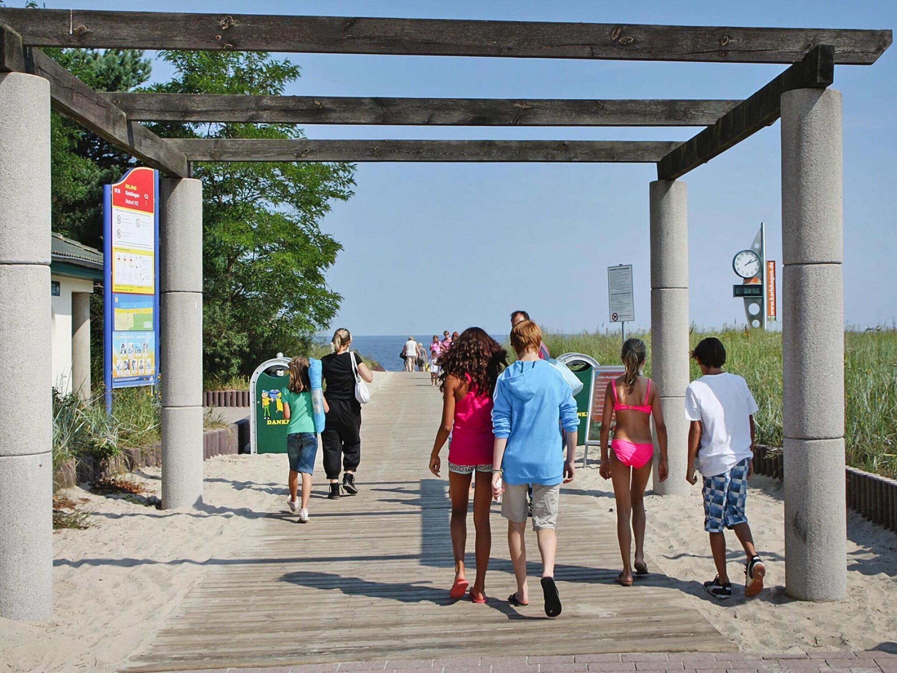 Une promenade en bois mène à une plage, et une pergola en bois est installée au-dessus.
