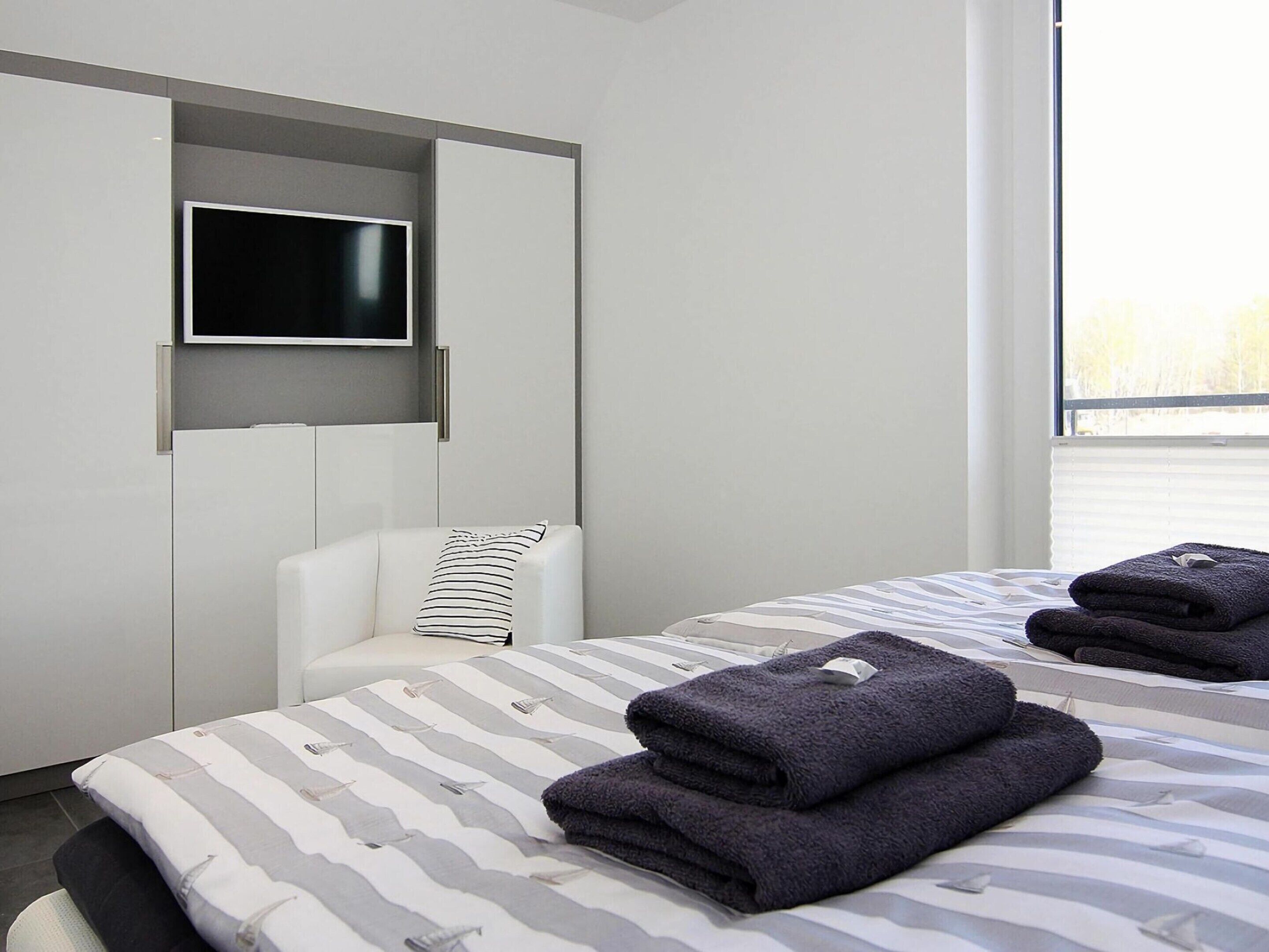 A modern hotel room with a bed, a TV mounted on a wall, and a window providing a view.