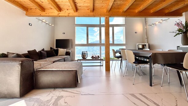 A modern living room with a large sectional sofa, a dining area with a table and chairs, and a large window offering a mountain view. - Casa Monti Neues Modernes Haus in den Bergen von Monti di Vairano (Monti di Vairano)