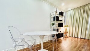 A modern dining area with a round white table, clear plastic chairs, and a wooden floor.