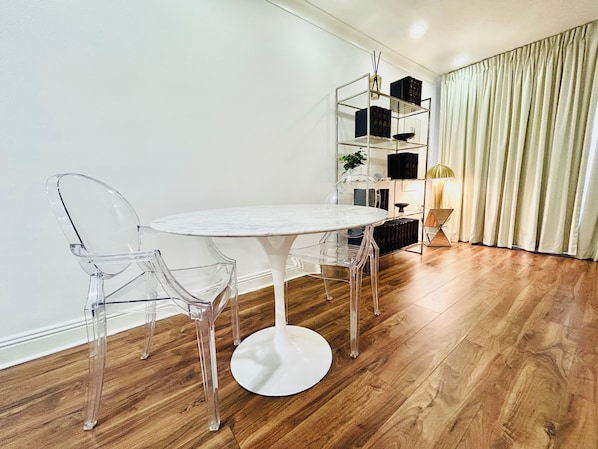 A modern dining area with a round white table, clear plastic chairs, and a wooden floor.