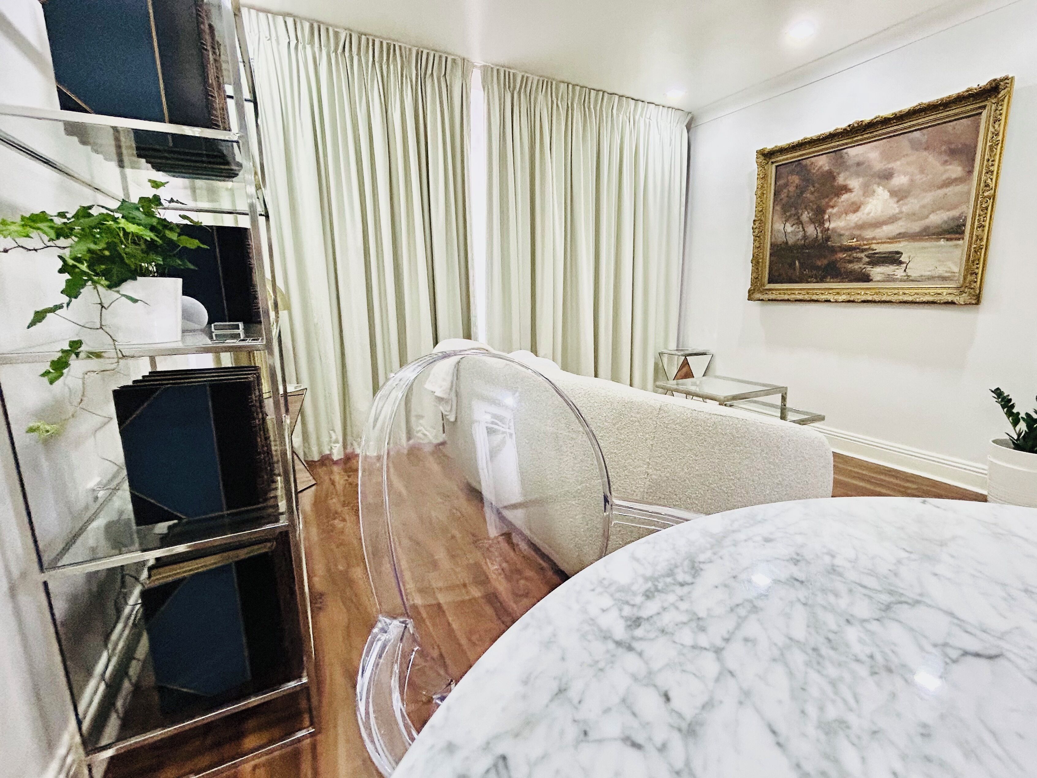 A modern hotel room with a marble table, a glass-walled bed, and a painting on the wall.