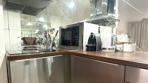 A modern kitchen with stainless steel appliances, a microwave, a coffee maker, and a glass cabinet.