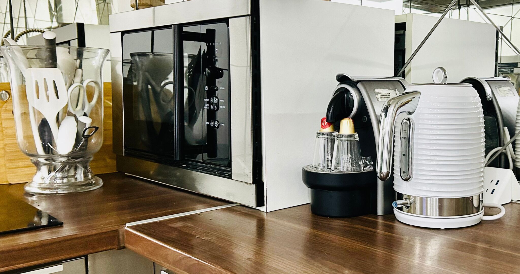 A kitchen with a microwave, a coffee maker, and a glass container with utensils.