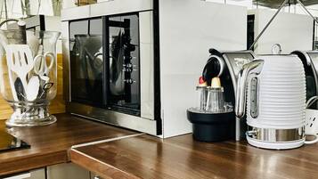A kitchen with a microwave, a coffee maker, and a glass container with utensils.