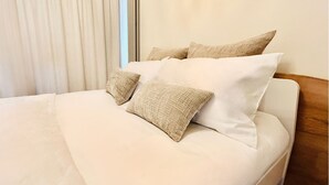 A neatly made bed with white linens and two textured beige pillows.