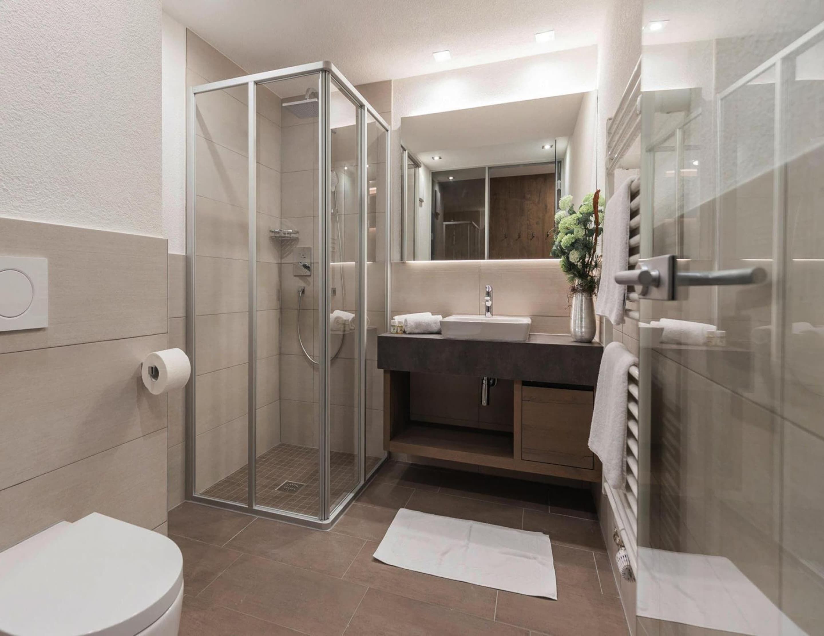 Ein modernes Badezimmer mit Duschkabine aus Glas, Toilette, Waschbecken mit Spiegel und Handtuchhalter.