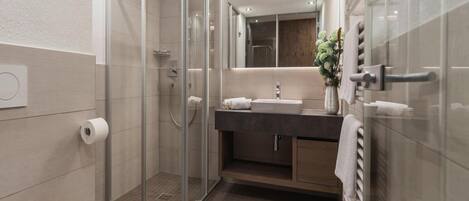 Ein modernes Badezimmer mit Duschkabine aus Glas, Toilette, Waschbecken mit Spiegel und Handtuchhalter.