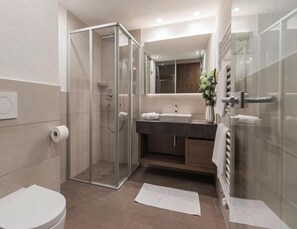 Ein modernes Badezimmer mit Duschkabine aus Glas, Toilette, Waschbecken mit Spiegel und Handtuchhalter.