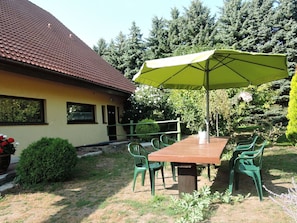 A patio with a table and chairs, a green umbrella, and a house with a tiled roof. - Holiday Home in Sulomino With Private Beach (gmina Wolin)