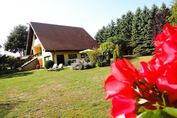 A two-story house with a sloped roof, a small porch with chairs, and a well-maintained lawn. - Holiday Home in Sulomino With Private Beach (gmina Wolin)