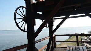 A wooden deck with a wheel structure, overlooking a calm body of water. - Holiday Home in Sulomino With Private Beach (gmina Wolin)