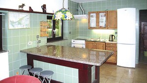 A kitchen with green tiled walls, wooden cabinets, a granite countertop island, and a red bar stool. - Holiday Home in Sulomino With Private Beach (gmina Wolin)