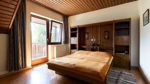 Une chambre avec un grand lit, des étagères encastrées en bois, un radiateur et une vue par la fenêtre.
