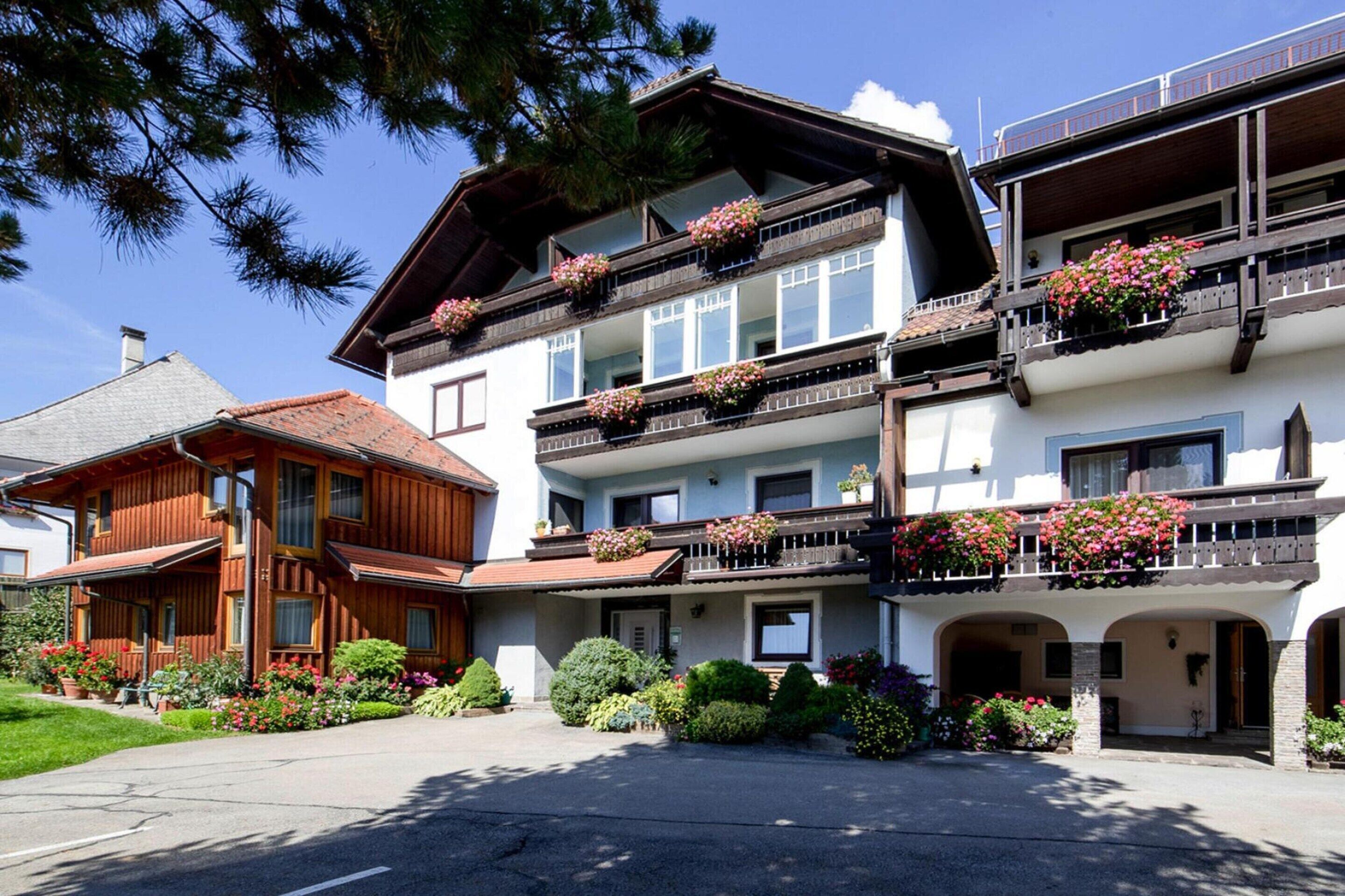Ein mehrstöckiges Hotel mit Balkonen, die mit Blumen geschmückt sind, ein gepflegter Garten und ein klarer Himmel.