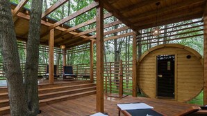 Eine Holzterrasse mit Liegestühlen und einer kleinen Bühne, umgeben von Bäumen.