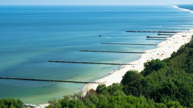 Ein Küstenstrand mit klarem Wasser, sandigem Ufer und einem Steg, der ins Meer führt.