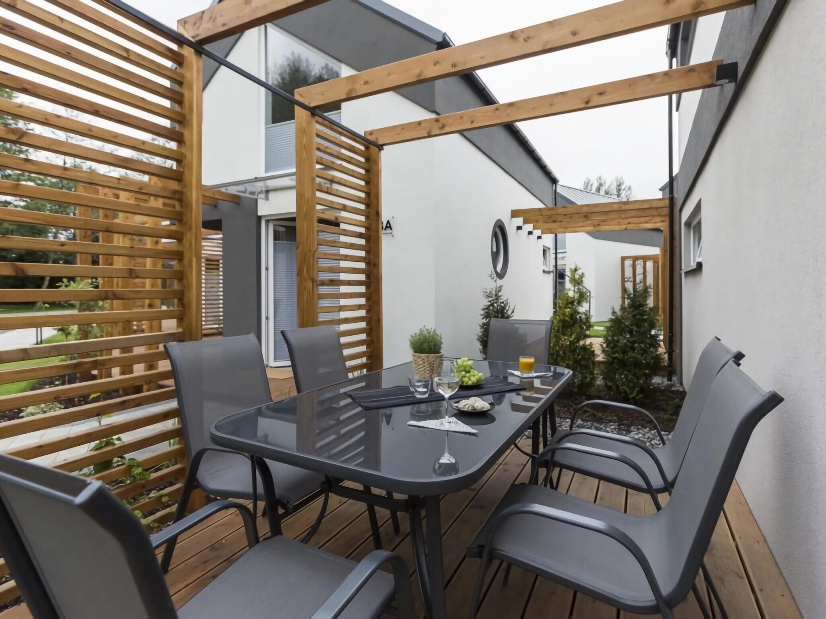 Een moderne buiten eethoek met een glazen tafel en metalen stoelen, omgeven door houten balken en een houten omheining.
