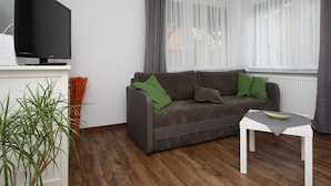 A modern living room with a grey sofa, a flat-screen TV, and a small white table. - Ferienhaus mit Wasserblick, Lubben (Lübben (Spreewald))