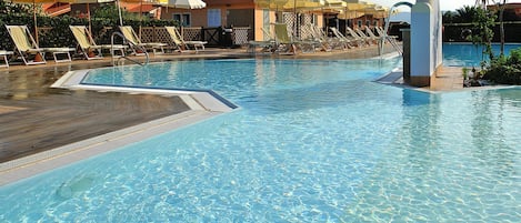 A swimming pool with clear water, surrounded by sun loungers and umbrellas.